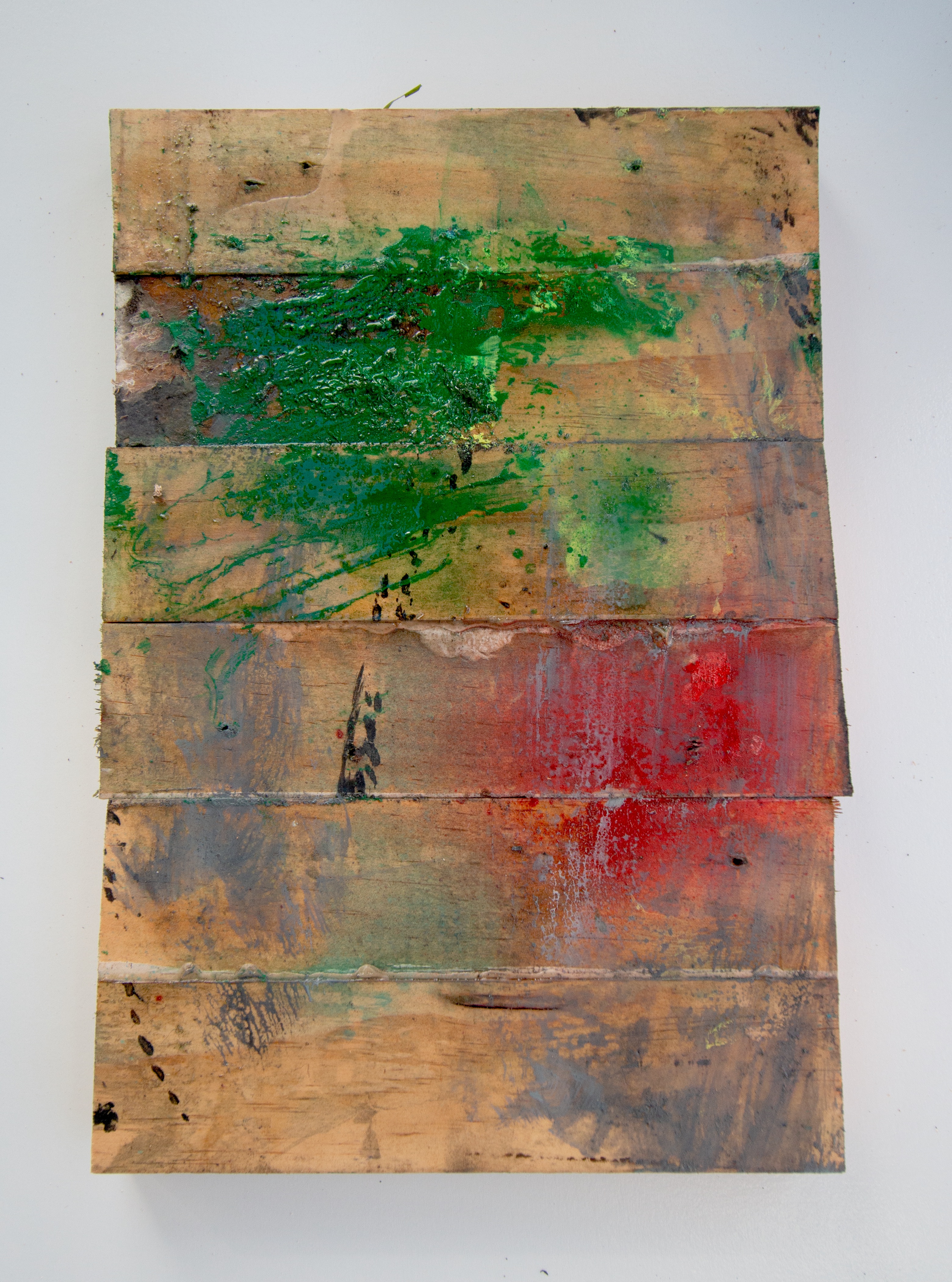 Portrait combine of horizontal wood slats in raw timber tone. A vivid green splatter pools near the top edge; a centred red bloom in the middle band; sparse black drips at lower left.